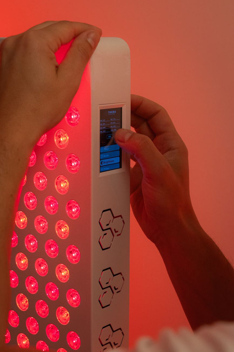 Mãos a ajustar a intensidade no ecrã tátil do painel de luz vermelha TheraPRO