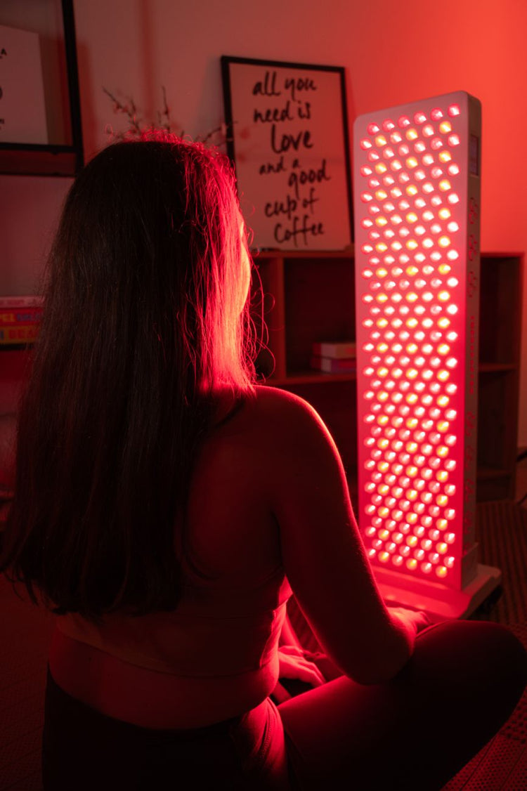 Mulher sentada em frente a um painel TheraPRO de corpo inteiro durante uma sessão de terapia de luz vermelha em casa