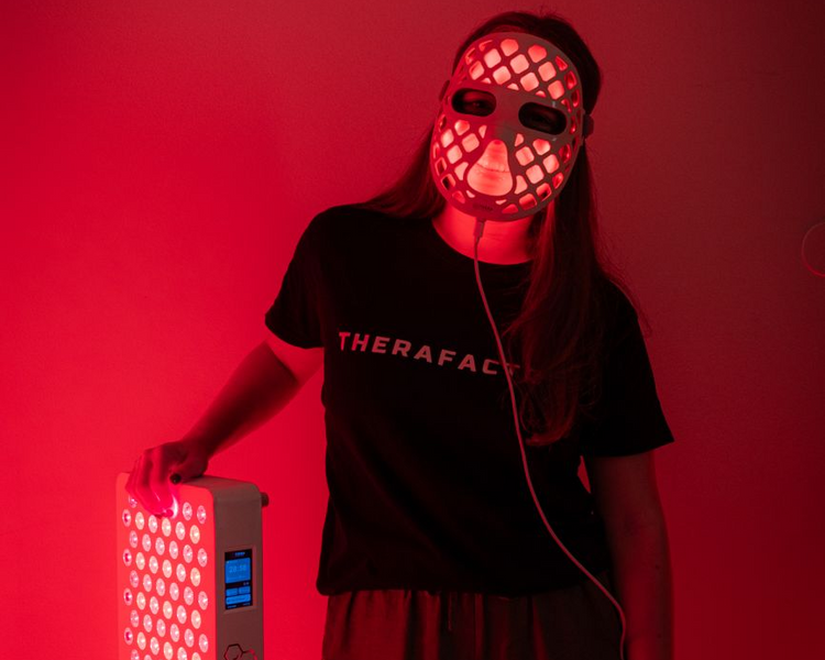 Mulher com a máscara TheraLUMI FaceMesh acesa e a mão sobre um painel TheraPRO